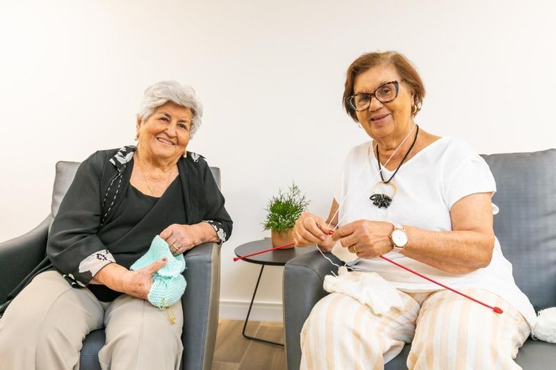 Duas residentes conversam enquanto fazem tricô